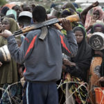 Flüchtlinge warten hinter ausgerolltem Springdraht auf die Verteilung der täglichen Reisrationen. Im Vordergrund ein Security Guard der Camp-Verwaltung.