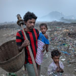 Bei Tagesanbruch geht der Waste-Picker Durgarao Potluri (28 Jahre) mit seinen beiden Kindern Sudharani (3 Jahre) und David (5 Jahre) auf den alten, unter starker Rauchentwicklung schwelenden Teil der Müllkippe. Vater Durgarao Potluri hat die Kinder lieber unter seiner Aufsicht, als dass die Kinder allein auf dem gefährlichen Areal der Müllkippe spielen.